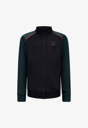 Zwarte jas met groene mouwen, rits aan de voorkant, hoge kraag en zijzakken. Heeft rode accentstiksels en een logo-patch op de borst.