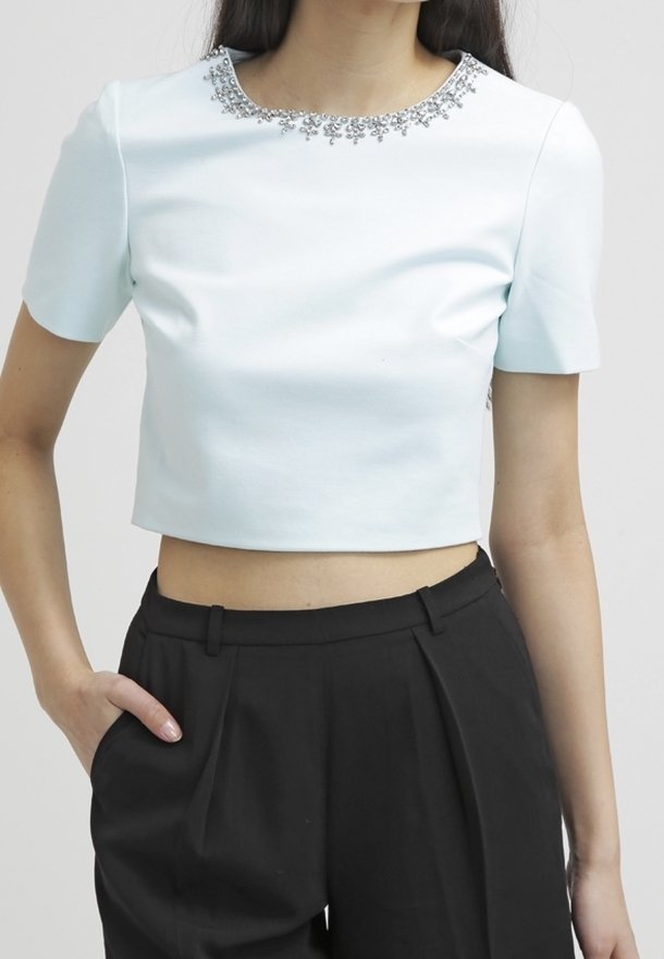 Cropped light blue top with short sleeves, embellished neckline, smooth texture, paired with high-waisted black trousers.