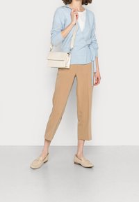 Jasnoniebieski sweter z wiązaniem, kremowa torba o teksturowej powierzchni, beżowe spodnie w stylu tapered oraz beżowe loafersy. Prosty i nowoczesny design stroju.