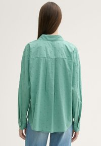 Camisa de manga larga verde menta con puntos de textura, puños abotonados y yugo trasero. La tela parece ligera y suave.