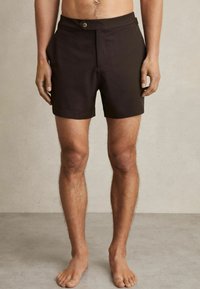 Shorts maro închis dintr-un material neted, cu închidere cu un buton în față, buzunare laterale și o tăietură clasică care se oprește deasupra genunchiului.