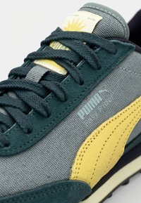 Läheltä kuvattu Puma Easy Rider -lenkkari, jossa on teal-väriset nauhat, kangasylä ja keltainen nahkaraidat sivussa.