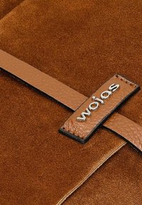 Materiale in suede marrone con una cinturino in pelle liscia. Presenta un'etichetta con logo in tonalità argentata e dettagli di cucitura a contrasto lungo i bordi.