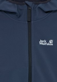 Close-up of navy blue jacket front with black zipper and white Jack Wolfskin logo featuring a paw print on the right chest.