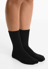 Zwarte katoenen sokken met ribbeltextuur, met een boord tot halverwege het onderbeen, naadloze teen en een gladde afwerking. Voeten zij aan zij geplaatst.