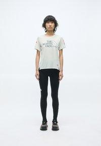 T-shirt gris clair à manches courtes avec le logo "The North Face", associé à un legging noir et des chaussures de trail noires avec des accents colorés.