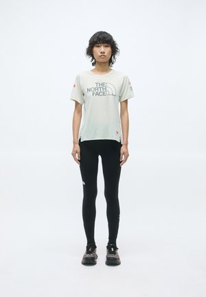 T-shirt gris clair à manches courtes avec le logo "The North Face", associé à un legging noir et des chaussures de trail noires avec des accents colorés.