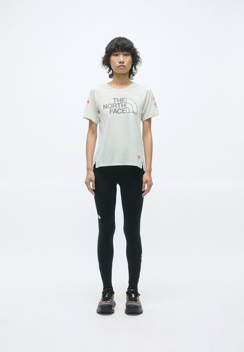 T-shirt gris clair à manches courtes avec le logo "The North Face", associé à un legging noir et des chaussures de trail noires avec des accents colorés.