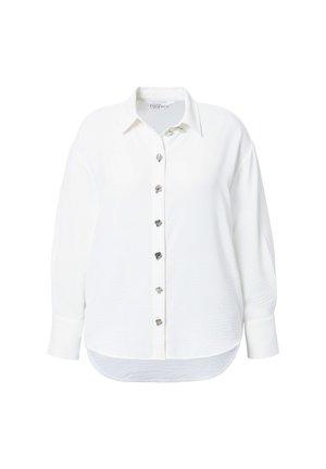 Camicia bianca a maniche lunghe con bottoni a forma di cuore argentati lungo il davanti e un orlo arrotondato nella parte inferiore.
