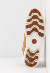 Suela de bota marrón claro con patrón de banda de rodadura blanco y marrón, con el logo de Timberland y la impresión de la tecnología SensorFlex.