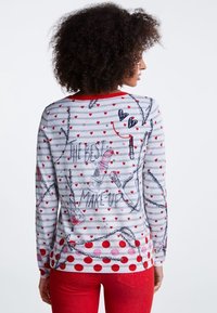 Grå langærmet sweater med røde prikker og hjerte mønstre, med grafik af læbestift og makeup børste, rød halsudskæring og struktureret stof.