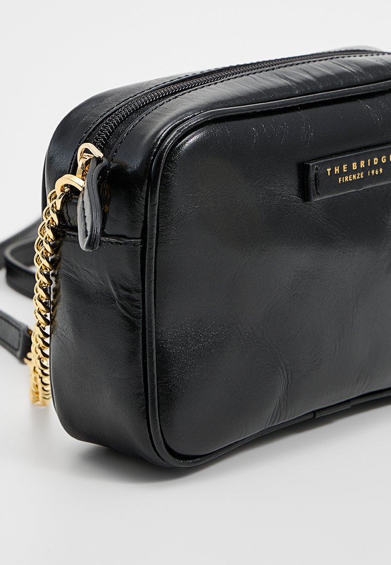 Borsa a tracolla in pelle nera con forma rettangolare, hardware dorato, chiusura con zip e dettaglio a catena sulla tracolla. Texture morbida, design minimalista.