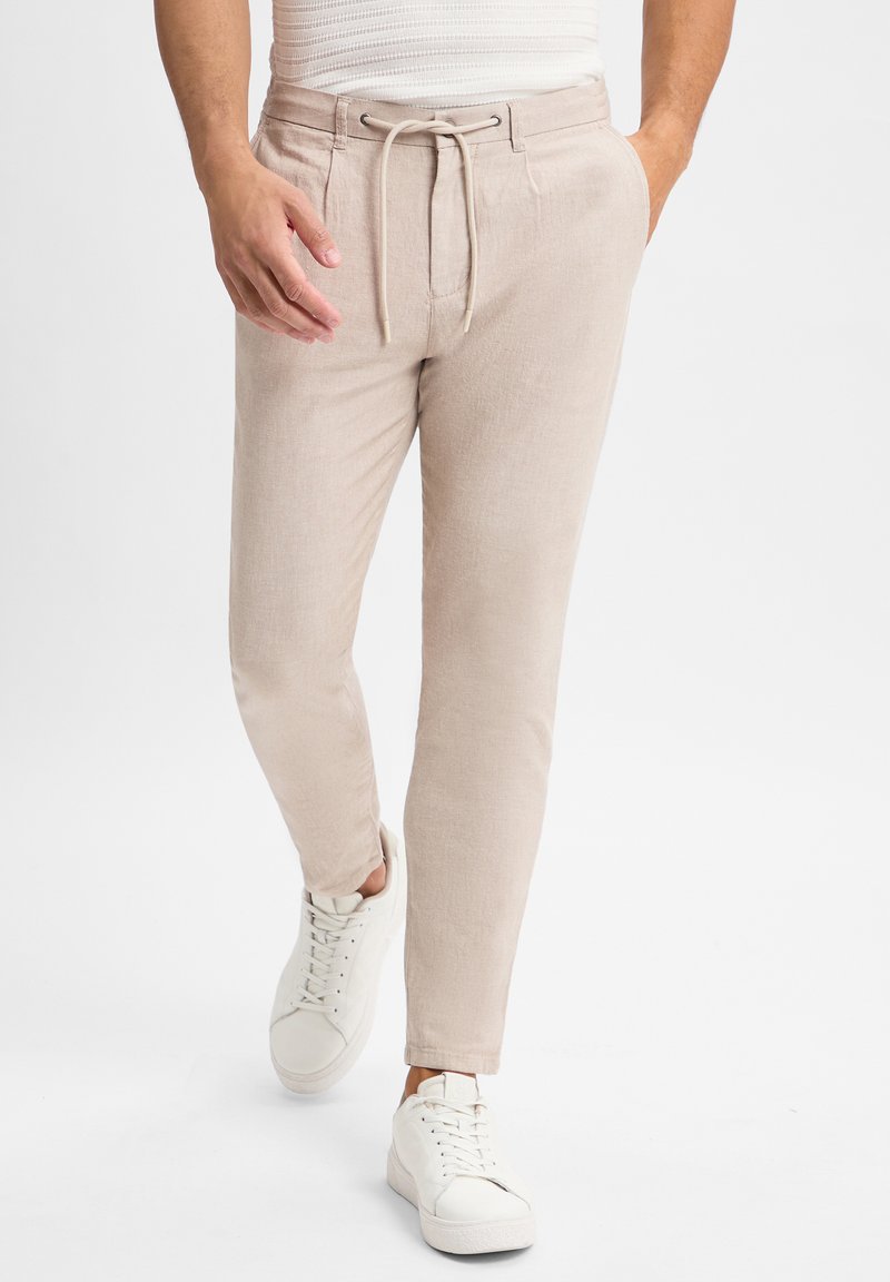 Lichtbeige, slim-fit broek met een trekkoord in de taille, vervaardigd van textuurstof. Gecombineerd met witte sneakers voor een casual uitstraling.