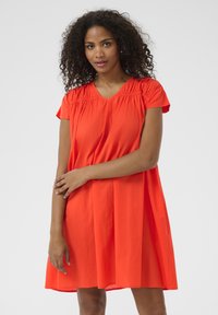 Kurzärmliges rotes Kleid mit V-Ausschnitt und Raffung an den Schultern, das einen lockeren Schnitt und eine glatte Textur aufweist.