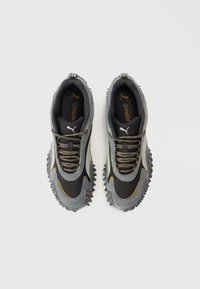 Grijze en zwarte sportschoenen met gestructureerde stof, een veterontwerp en een rubberen zool met spikes. Goudkleurig logo op de binnenzool.