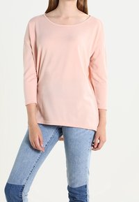 Helles rosa, lockeres Oberteil mit weitem Ausschnitt und Dreiviertelärmeln, kombiniert mit blauen Jeans in einem farbblockierten Design.