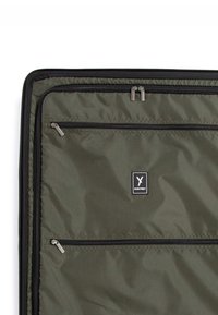 Intérieur d'une valise en tissu vert foncé avec plusieurs compartiments zippés et un patch logo "Suri Frey" au centre.