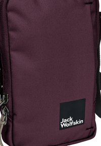 Paarse stoffen tas met een gestructureerde afwerking, voorzien van een zwart logo label. Bevat een ritssluiting en grijze hardware, compact rechthoekig ontwerp.