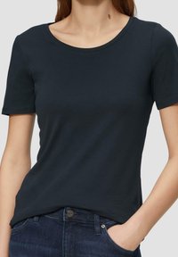 Donkerblauw t-shirt met een ronde hals en korte mouwen, gemaakt van gladde stof, gecombineerd met donkere spijkerbroek met een knoopdetail.