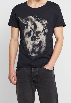 Czarna koszulka z białym, dymnym motywem czaszki i napisem "Jack & Jones Los Angeles", noszona przez osobę w ciemnoszarych dżinsach.