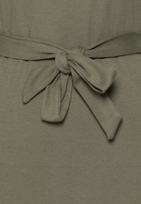 Tissu vert olive à texture côtelée orné d'un nœud noué à la taille, créant une silhouette lisse et structurée.