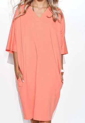 Koralrød oversized kjole med V-hals, korte ærmer, sidelommer og blød tekstur, med et enkelt, pynteløst design uden mønstre.