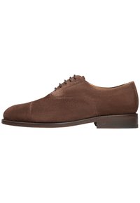 Scarpa oxford in suede marrone con punta tondeggiante, chiusura con sei occhielli e tacco di legno piatto. Texture liscia e dettagli di cucitura minimi.