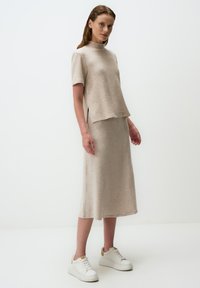 Ensemble en tricot beige comprenant un haut à col montant et manches courtes, associé à une jupe longue assortie, le tout agrémenté de baskets blanches pour une allure décontractée.