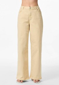 Pantalons larges beiges en mélange de coton. Comprend une taille haute, cinq poches et une fermeture à bouton. Texture lisse et coupe décontractée.