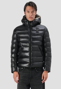 Giacca a vento nera con finitura lucida, dotata di zip frontale, cappuccio e tasche laterali. Design trapuntato con sezioni orizzontali ben evidenti.