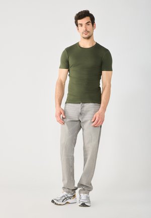 Oliven grønn kortermet tettsittende T-skjorte kombinert med lysegrå jeans og grå joggesko. Enkelt design, ingen synlige mønstre eller detaljer.