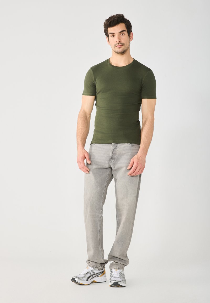 Camiseta ajustada de manga corta en verde olivo combinada con jeans gris claro y zapatillas de correr grises. Diseño sencillo, sin patrones ni acentos visibles.