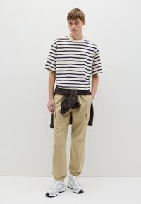 Camisa de manga corta a rayas en crema y azul marino, combinada con pantalones cargo caquis. El calzado son zapatillas deportivas blancas. Conjunto informal con detalles prácticos.