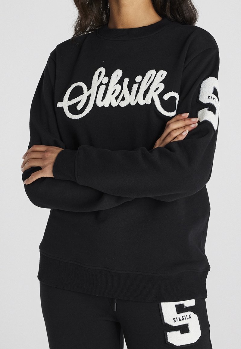 Czarna bluza z białym haftem "Siksilk" z przodu oraz białą łatką z numerem 5 na prawym rękawie. Miękka, luźna forma.