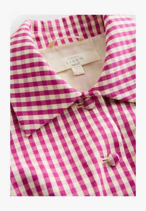 Cămașă din in cu model în carouri roz și crem. Are guler tip cămașă și închidere cu nasturi. Etichetă interioară vizibilă cu informații de întreținere.
