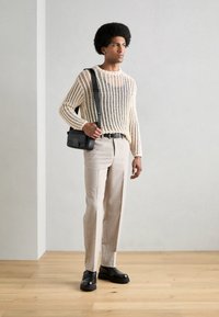Knit cream sweater with open pattern, light beige tailored pants, black belt, and small black crossbody bag; paired with black shoes.