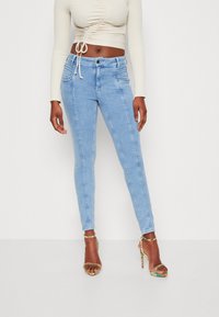 Los jeans skinny azul claro presentan una textura de denim suave, un diseño de cinco bolsillos y una cintura de altura media, combinados con sandalias de tacón alto con tiras.