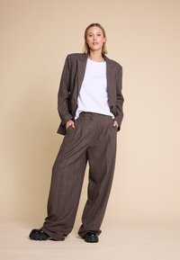 Brun rutete dress med en oversized blazer og vide bukser, båret over en hvit t-skjorte, komplementert av svarte kraftige sko.