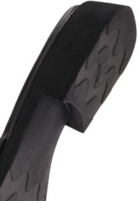 Suela de zapato negra con agarre de goma texturizada. Presenta un patrón ondulado en la parte inferior para tracción y un ligero tacón para elevación. Material de goma.