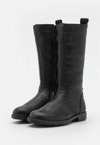 Bottes en cuir noir montantes avec une finition lisse, des zips sur les côtés et des accents perforés décoratifs sur les côtés. Semelles en caoutchouc plates.