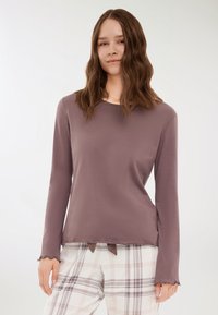 Maglia a maniche lunghe color malva con scollatura rotonda e orlo ondulato, abbinata a pantaloni da pigiama a quadri nei toni del bianco, rosa e grigio.