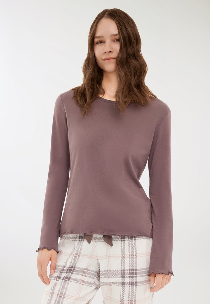 Maglia a maniche lunghe color malva con scollatura rotonda e orlo ondulato, abbinata a pantaloni da pigiama a quadri nei toni del bianco, rosa e grigio.