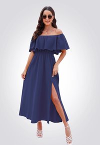 Abito lungo blu navy con spalle scoperte, maniche a volant, vita elastica e spacco alto fino alla coscia. Presenta un tessuto leggero e un design fluido.