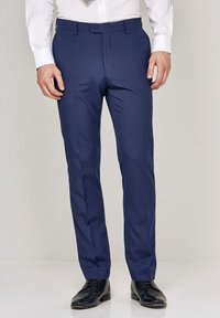 Hlače slim fit v temno modri barvi, izdelane iz gladkega materiala. Imajo ravno sprednje zareze, stranske žepe in zanke za pas, v kombinaciji s črnimi čevlji.