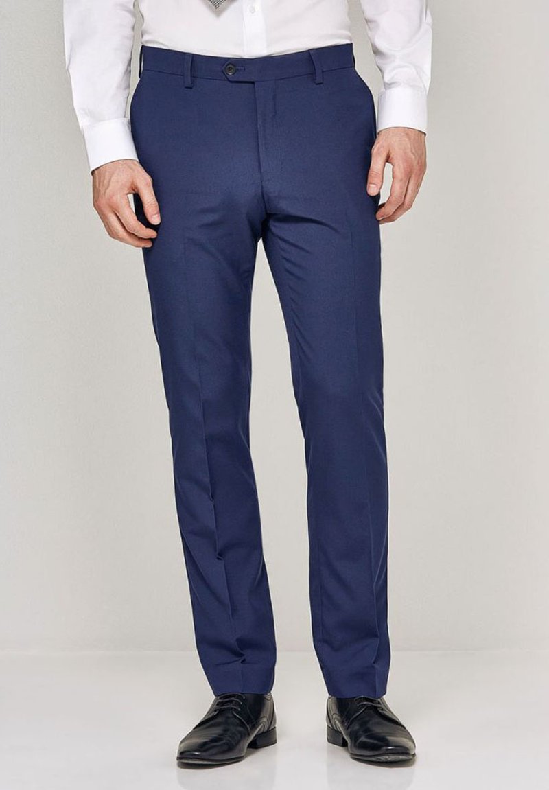 Hlače slim fit v temno modri barvi, izdelane iz gladkega materiala. Imajo ravno sprednje zareze, stranske žepe in zanke za pas, v kombinaciji s črnimi čevlji.