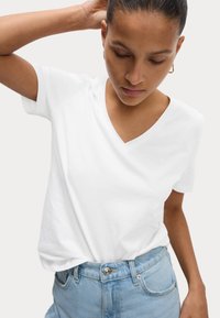 T-shirt bianca con scollo a V e maniche corte, realizzata in morbido cotone. Abbinata a jeans di denim blu chiaro, con un bottone in vita.