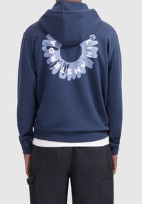Marineblauwe hoodie met een ronde witte graphic op de achterkant, gemaakt van een zachte, gestructureerde stof en met ribgebreide mouwen en zoom.
