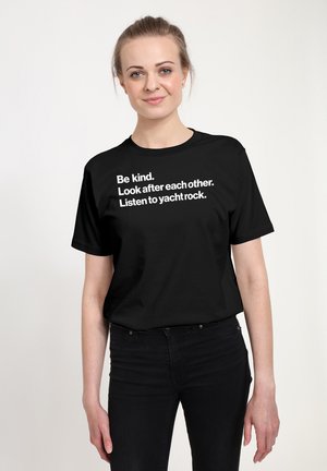 Sort bomuld t-shirt med hvid tekst: "Vær venlig. Tag vare på hinanden. Lyt til yacht rock." Rund hals, korte ærmer, afslappet pasform.