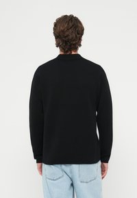 Czarna koszulka polo z długim rękawem i kołnierzykiem, wykonana z gładkiej tkaniny. Tył ma prosty design bez dodatkowych zdobień.