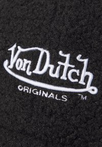 Black textured fabric with embroidered white "Von Dutch" logo and "ORIGINALS" text below, featuring a soft, fluffy surface.